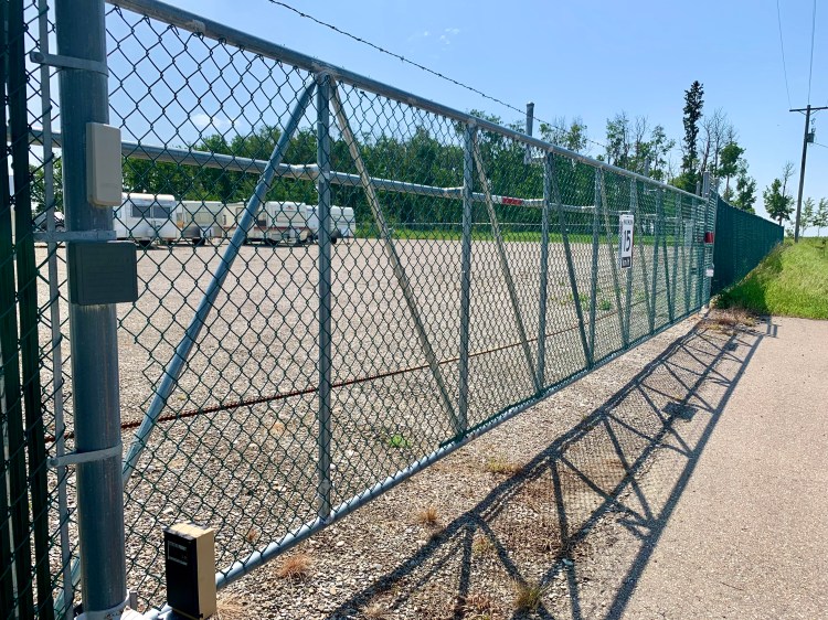 View of secure gated entrance with chain-link fence at Trailing West RV and Boat Storage near Sundre, Alberta, providing swipe card access to the fenced gravel lot for RVs, trailers, and boats.
