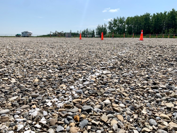 Wide gravel parking lot at Trailing West RV and Boat Storage between Sundre and Olds, Alberta, offering spacious, level stalls for RVs, trailers, and boats with secure fencing and open access lanes.